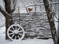Old village fence. Snow, winter. Cart wheel