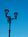 Old vintage black decorative lantern with clear glass on pillar. Three street lamps on one pole. Blue sunny sky. City Royalty Free Stock Photo