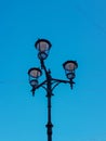 Old vintage black decorative lantern with clear glass on pillar. Three street lamps on one pole. Sunny blue sky gradient Royalty Free Stock Photo