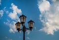Old vintage black decorative lantern with clear glass on pillar. Three street lamps on one pole. Sunny blue sky Royalty Free Stock Photo