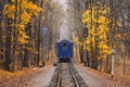 Old vintage blue railway train back view on the track rails goes away. Railroad single track through the woods in autumn. Fall Royalty Free Stock Photo