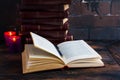 Old vintage books laying like a tower on a dark wooden table and one open book. Red hard cover, burning candle flames Royalty Free Stock Photo