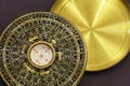 Old vintage chinese compass used in feng shui, golden item with hieroglyphs and cover, on dark background.