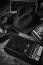 Old vintage cinematic noir scene, detective`s desk with a hat, telephone, camera, portable cassette recorder, and whisky