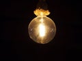 Old vintage dusty edison light bulb hanging on a rope fixture glowing against a black background