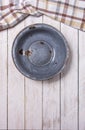 Old vintage enameled rusty bowl on white wooden desk and checkered kitchen cloth on top side. Vertical photo.