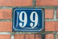 Old vintage house address blue metal number 99 ninety nine on the brick facade of residential building exterior wall on the street Royalty Free Stock Photo