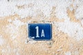 Old vintage house address blue metal number 1 A one on the plaster facade of abandoned home exterior wall on the street side