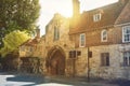 Old vintage medieval beautiful stone british house with tile roof and bright windows, and big trees near the asphalt road in warm Royalty Free Stock Photo