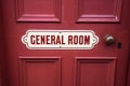 Old vintage metal painted sign saying General Room on a painted red wooden background with brass door handle Royalty Free Stock Photo