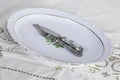 Old vintage silver knife and fork set on empty oval plate on the table covered with white embroidered tablecloth. Grandparents or