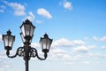 Old vintage street lamp post or lantern with light bulbs against a beautiful blue sky with white clouds background Royalty Free Stock Photo