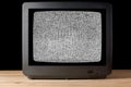 Old vintage TV set televisor on wooden table againt black background with no signal television grainy noise effect on the screen. Royalty Free Stock Photo