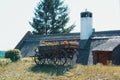 An old vintage wooden cart filled with bright red flowers standing on a green grassy hill beside the thatched roof of a tradition Royalty Free Stock Photo