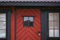 An old vintage wooden front door with window on a red country house. Facade exterior, closeup view. Retro countryside