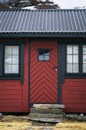 An old vintage wooden front door with window on a red country house. Facade exterior. Retro Scandinavian countryside