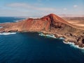 Old volcano with red rock and Atlantic ocean near La Santa, Lanzarote. Aerial view