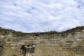 An old wall of an ancient stone building destroyed by time with dry grass on the background of a cloudy sky. Copy space. Royalty Free Stock Photo