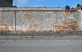 Old wall with peeled plaster and exposed bricks. Porphyry sidewalk and asphalt road in front,