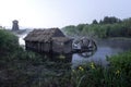 An old water mill with a wheel on the river. In the background is an old windmill. Early morning on the river covered Royalty Free Stock Photo