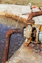 Old water valve. An rusty water valve in a puddle of flowing water. Large and rusty faulty leaking valve in close-up of an outdoor Royalty Free Stock Photo