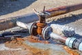 Old water valve. An rusty water valve in a puddle of flowing water. Large and rusty faulty leaking valve in close-up of an outdoor Royalty Free Stock Photo