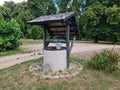 An old water well with a roof over a wooden gate and an empty bucket in the garden Royalty Free Stock Photo