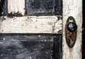 Old weathered antique beat-up wood panel door with chipped peeling paint and black porcelain doorknob and rusty plate