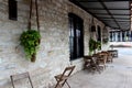 Old stone exterior wall of building with rows of mismatched chairs and tables set against it