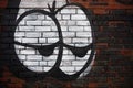 Old weathered red and black brick wall with eyes graffiti