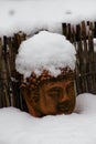 Old weathered terracotta buddha head covered with snow