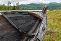 Old and weathered wooden boat wreck laying on the ground in beautiful norwegian landscape with mountains in the background.