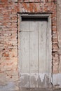 An old weathered wooden door is closed. The facade is made of old brick from which the plaster is falling. The image is in Royalty Free Stock Photo