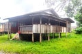 Old and weathered wooden house with pillars and stairs made out of bricks surrounded with grass.