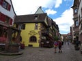 Old well decorated with flowers and houses with colorful facades in the streets of Riquewihr