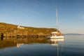 Old white abandoned Church Agios Ioannis on dramatic cliff with a sailboat anchored in a bay, on Kithnos Island, Greece