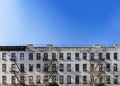 Old white brick apartment building with windows and fire escapes and an empty blue sky background overhead in New York City Royalty Free Stock Photo