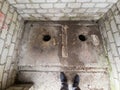 Old white brick toilet with two holes in the ground. Man`s feets Royalty Free Stock Photo