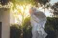 Old white cupid sculpture or statue standing in outdoor garden.