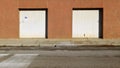 Old white garage doors on brown building facade at the roadside. Concrete sidewalk and city street in front Royalty Free Stock Photo