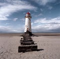 An old white lighthouse with a red roof on a sandy beach with the sea and sky in the background Royalty Free Stock Photo