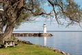 Old white lighthouse on the lake on a sunny day. Bright blue sky, wooden table and bench on the shore, beautiful summer landscape. Royalty Free Stock Photo