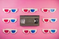 Old white paper 3d glasses with blue red lenses and black videotape on pink background. Retro video cassette with