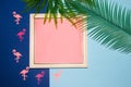 old white retro frame with pink copy space, around the frame flamingo and jungle leaves on a dark and pastel blue background Royalty Free Stock Photo