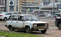 An old white rusty car is parked on the street