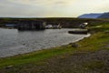 Old white rusty iron boats on green grassy shore of small round bay, with barn on the water. Blue mountains Royalty Free Stock Photo