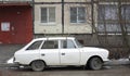 An old white Soviet car is parked in the courtyard of a residential building