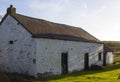An old whitewashed stone built Irish Cottage with a small annex roofed with bangor Blue roofing tiles and rusting corrugated tin s
