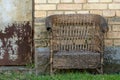 An old wicker chair stands outside near a brick house. Free seat on the armchair. A cozy place to relax in nature