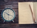 Old wind clock with notebook and pencil on wood table in vintage color scheme Royalty Free Stock Photo